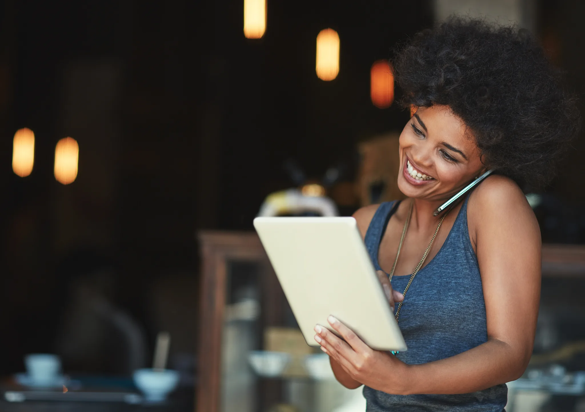 Shot of a young woman using a digital tablet while talking on the phone at a cafe